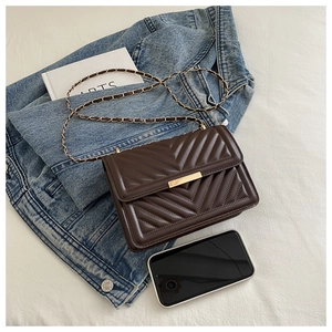 Close-up of brown quilted crossbody bag with gold hardware and chain strap on denim