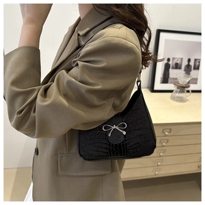 Borsa nera in simil coccodrillo con fiocco argento indossata su un blazer beige