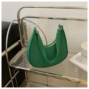 Green hobo bag with crocodile pattern and gold hardware on a modern minimalist shelf