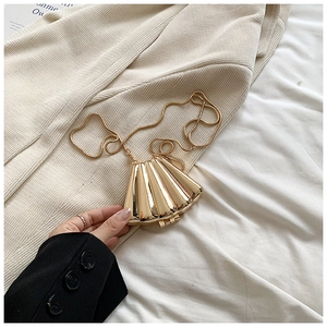 Detail of a golden shell-shaped clutch bag with fine snake chain on beige fabric
