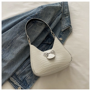 Détail du sac blanc motif crocodile avec nœud argenté sur fond en jean bleu