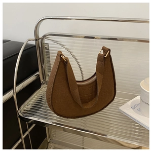 Close-up of brown crocodile embossed moon bag with gold zipper on a modern display