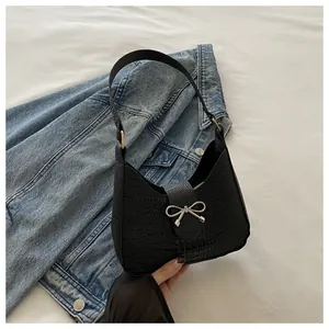 Détail du sac à bandoulière noir en cuir croco avec boucle nœud argentée sur jean