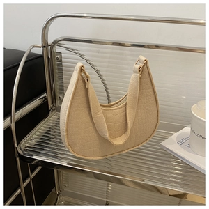 Detail showing beige moon bag with crocodile embossing on a modern shelf