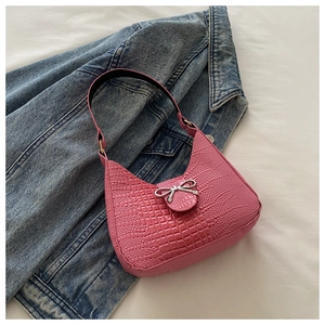 Gros plan détaillé du motif crocodile rose et du nœud argenté sur le sac à bandoulière