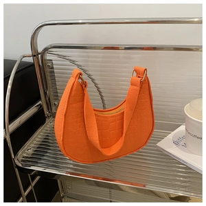 Close-up of vibrant orange crescent handbag with crocodile texture on a glass stand