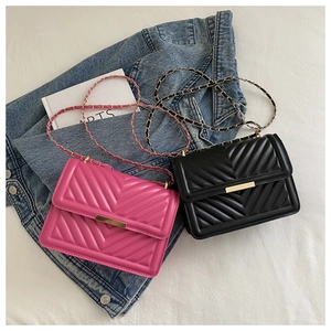 Detail of chevron quilted crossbody bags in fuchsia and black with golden chain straps