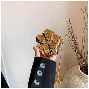 Detail of a golden flower-shaped evening clutch bag with metallic finish and chain strap