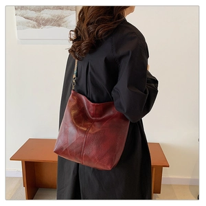 Model wearing a burgundy tote bag with vintage patterned strap in a cozy indoor setting