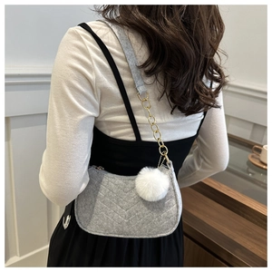 Detail of grey felt shoulder bag with V-quilted stitching and white fuzzy pompom charm