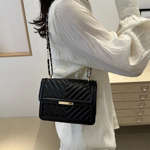 Modern black quilted crossbody bag with gold buckle and chain strap on female model