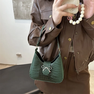 Sac hobo vert foncé motif crocodile avec nœud argenté porté à l'épaule sur modèle