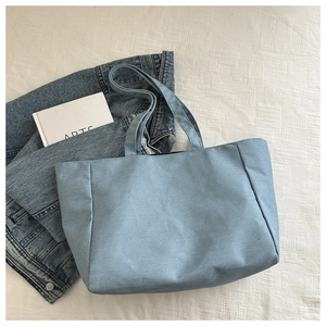 Gros plan du sac fourre-tout en toile bleu clair sur draps blancs avec veste en jean