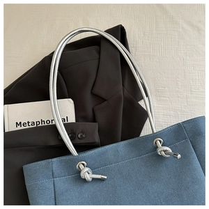 Détail du sac cabas en denim bleu avec anses métalliques spirales argentées