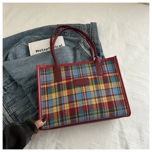 Close-up of multicolored plaid tote bag with red leather handles on denim background