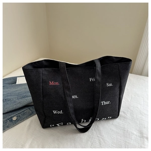 Close-up of black denim tote bag featuring white and red weekday typography print