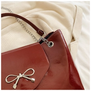 Détail du sac en cuir verni bordeaux avec nœud métallique et surpiqûres blanches
