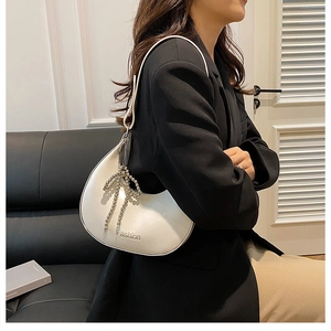Detail of white crescent shoulder bag with metallic bead bow charm and Fashion logo