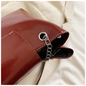 Détail du sac en cuir brillant bordeaux avec coutures blanches et chaîne argentée