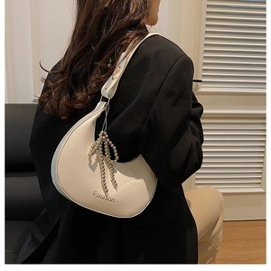 Close-up of beige crescent underarm bag with glossy finish and metal bow charm