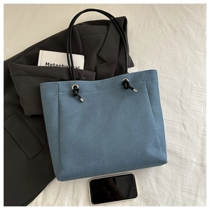 Détail du sac cabas en denim bleu avec anses cordes noires sur un bureau de travail