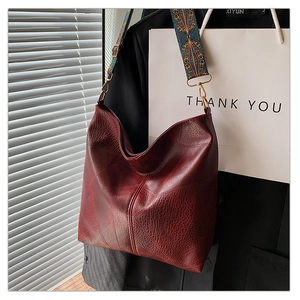 Close-up of deep red leather tote bag featuring a colorful ethnic embroidery wide strap
