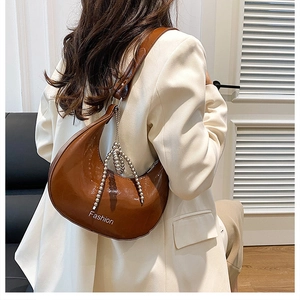 Detailed view of brown glossy crescent bag with metal bead chain and Fashion text