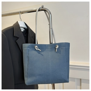 Détail d'un sac cabas en denim bleu avec bandoulières métalliques et nœuds argentés