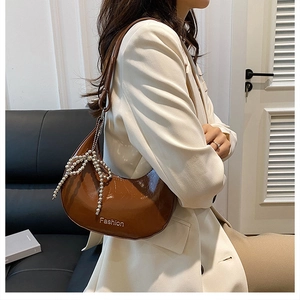 Detail of a brown glossy crescent bag with a pearl beaded bow charm on a leather sofa