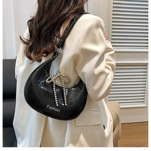Detail of black glossy hobo bag with silver beaded bow charm on white blazer