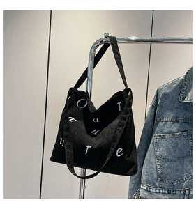 Détail d'un sac cabas en velours côtelé noir avec broderie blanche sur un support