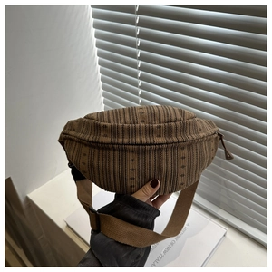 Détail d'un sac banane tissé à rayures marron avec bandoulière réglable et fermeture éclair