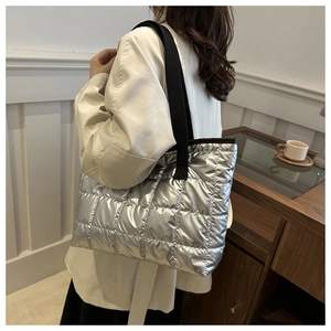 Sac cabas argenté matelassé avec large bandoulière noire porté à l'épaule pour femme