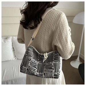 Detail of striped tote bag with rope knot zipper, worn with a beige knitted sweater