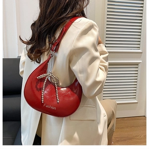 Detail of red patent leather half-moon bag featuring a silver bead bow charm on a shoulder