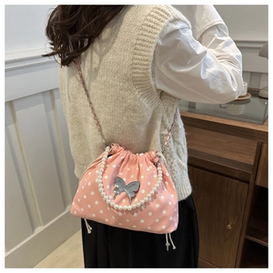 Pink polka dot drawstring bucket bag featuring a pearl handle and silver butterfly charm