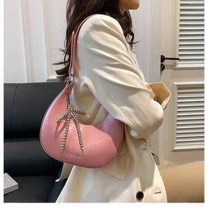 Detail view of pink hobo bag with Fashion text and beaded bow charm on model shoulder