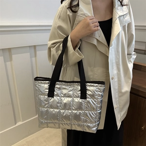 Sac fourre-tout matelassé argenté avec anses noires porté avec un trench-coat beige