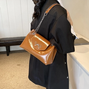 Sac fourre-tout chic en cuir verni caramel avec chaîne argentée et nœud porté par mannequin