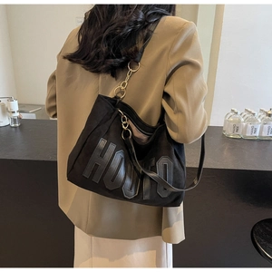 Detail view of large black slouchy tote bag with golden metal chain and HOUIO leather patch