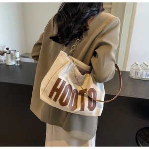 Detail of canvas tote bag with brown HOOTO leather patch and metal chain shoulder strap