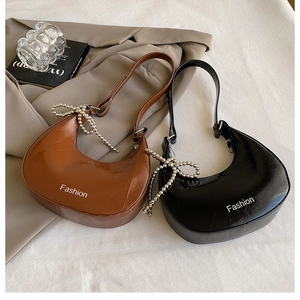 Detailed view of polished faux leather crescent bags in black and brown with pearl bows