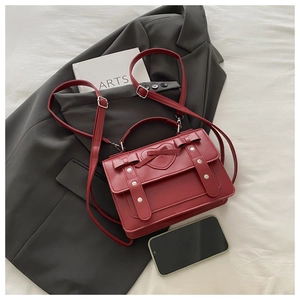Detail of red leather satchel with heart stitching, bow accents, and silver studs on a suit