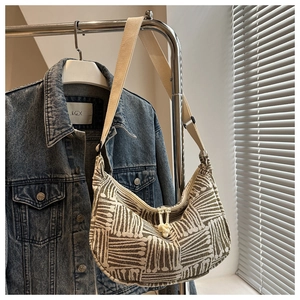 Detail of striped woven half-moon tote bag with green geometric patterns and knot zipper