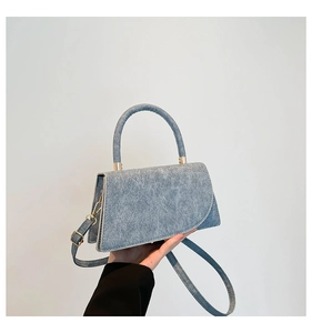 Dettaglio della borsa blu in denim con forma trapezoidale e finiture metalliche dorate