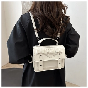 Detail of white leather backpack showing heart applique, bow, and adjustable straps
