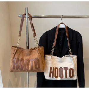 Detail of suede and canvas tote bags with HOOTO leather lettering and chain straps