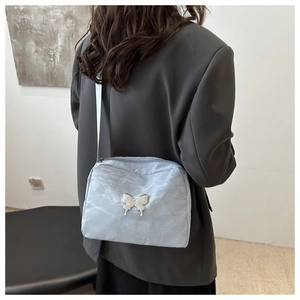 Detail of silver metallic crossbody bag with butterfly ornament worn by a model