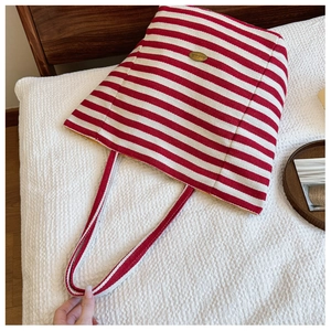 Detailed close-up of red and white striped canvas tote bag with elegant gold metal logo tag