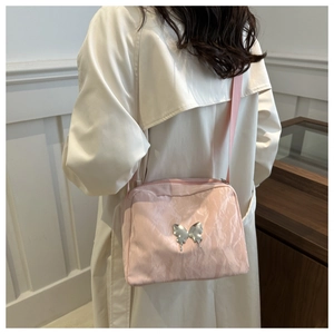Detail of light pink crossbody bag with pleated texture and silver butterfly buckle logo